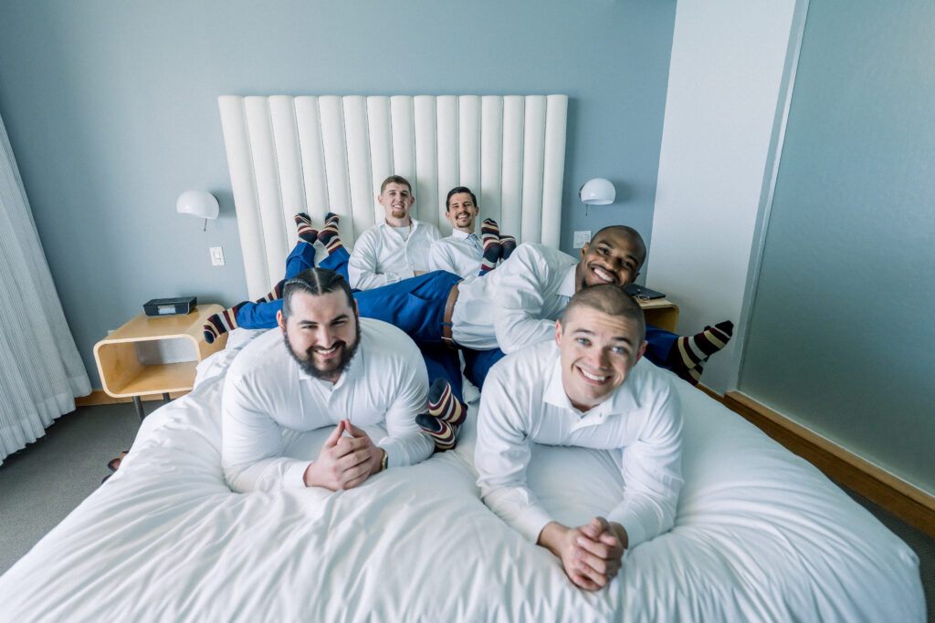 Groom and friends laying in bed before wedding